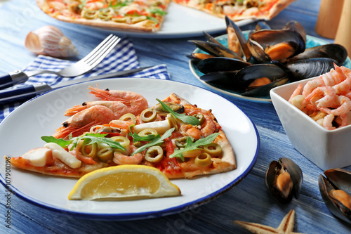 Pizza slice with seafood, red pepper and green olives on blue wooden table