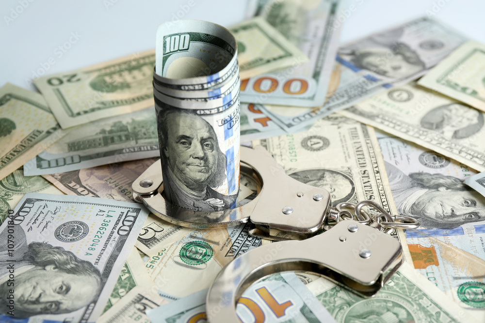 Fototapeta premium Handcuffs with rolled dollar banknote on paper background. Corruption concept