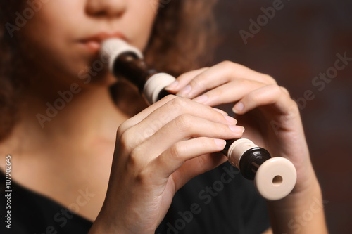 Beautiful young woman playing on recorder over brick wall background photo