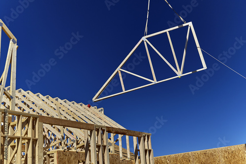 фотографія A wooden roof truss being lifted by a crane in the air for placement on the roof