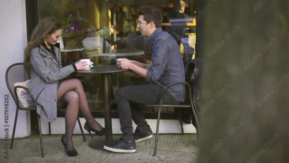 Camera dollies around tree to reveal Beautiful Man and Woman having tea date together on sidewalk outside chocolate shop Camera dollies around tree to reveal Beautiful Man and Woman having tea date together on sidewalk outside chocolate shop