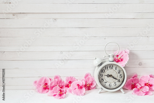 Fototapeta Naklejka Na Ścianę i Meble -  Background with white alarm clock and flowers pink orchid on whi