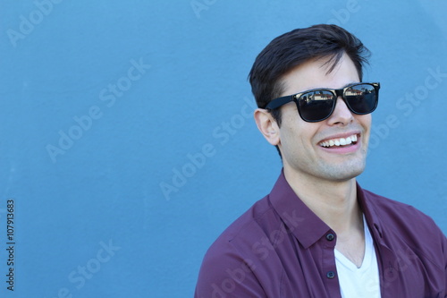 Headshot of a Caucasian man in his mid twenties with designer sunglasses taken against a plain blue background with copy space for adding text photo