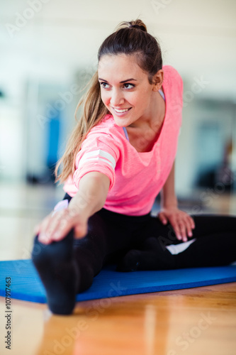 Young brunette european white caucasian girl exercising alone in gym with wooden floor doing yoga, pilates and fitness exercises