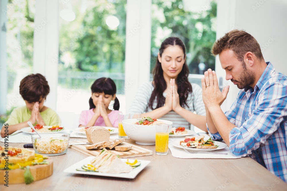 Family praying while sitting at dining table Family praying while sitting at dining table