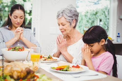 Mother and daughter with granny praying at dining table 