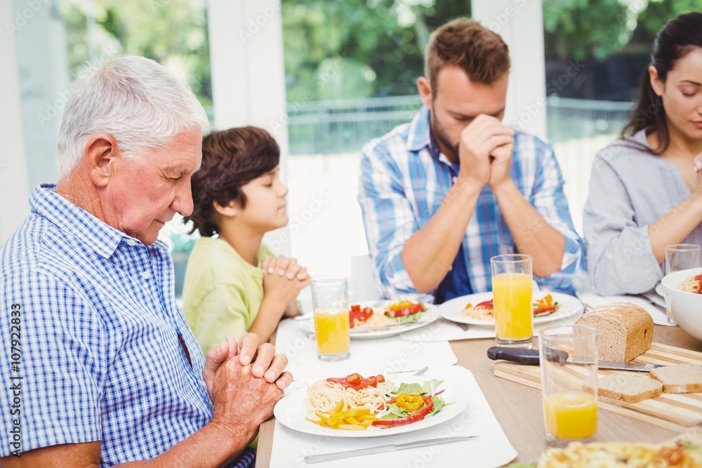 Multi generation family praying while sitting at dining table Multi generation family praying while sitting at dining table