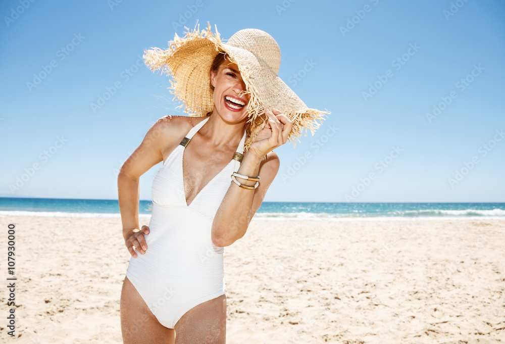 Smiling woman in swimsuit hiding in big straw hat at sandy beach Smiling woman in swimsuit hiding in big straw hat at sandy beach