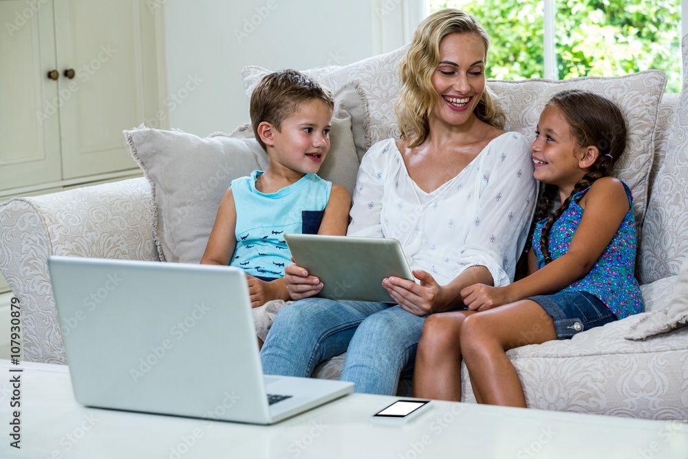 Mother sitting with daughter and son using tablet on sofa Mother sitting with daughter and son using tablet on sofa