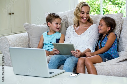Mother sitting with daughter and son using tablet on sofa