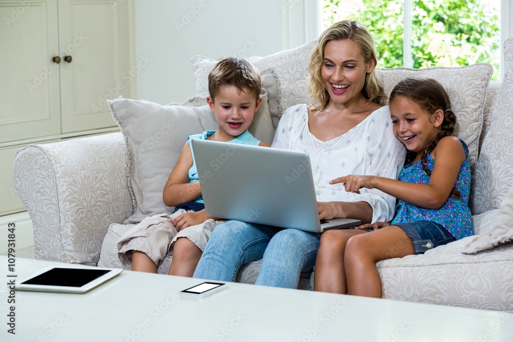 Cheerful children and mother using laptop on sofa Cheerful children and mother using laptop on sofa