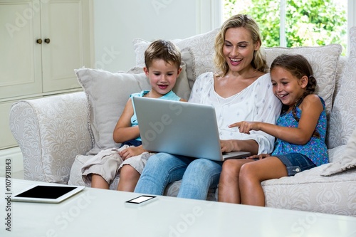 Cheerful children and mother using laptop on sofa