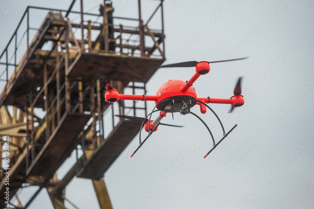 Red industrial drone flies over metal structures industrial faci