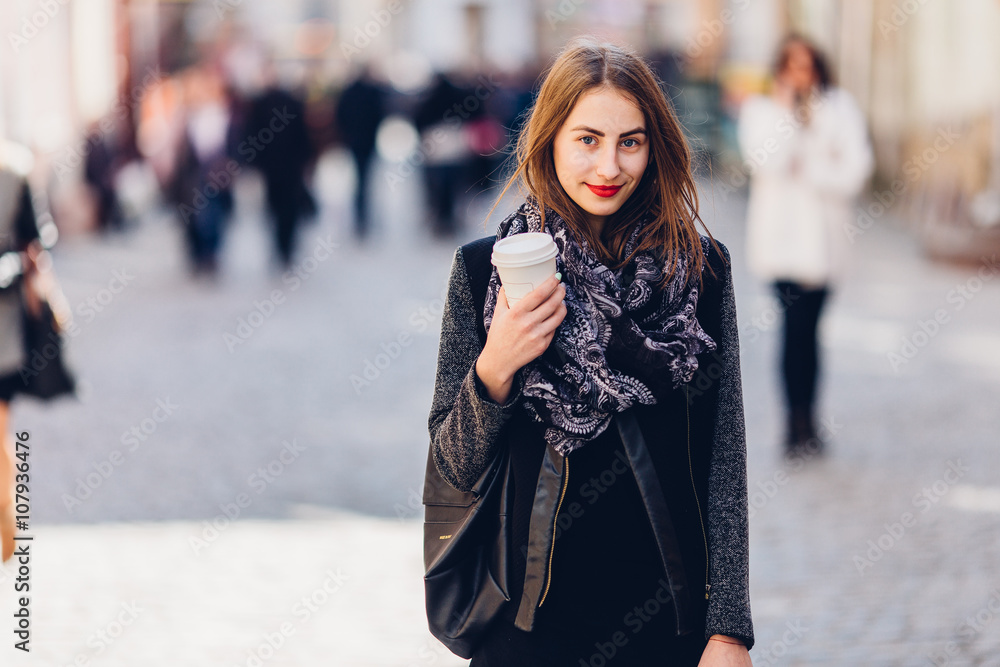 Fototapeta premium Young girl walking on the street with cup of hot coffee