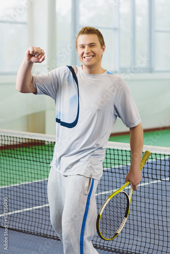 young man smiling and posing with tennis racket indoor © dreamsnavigator