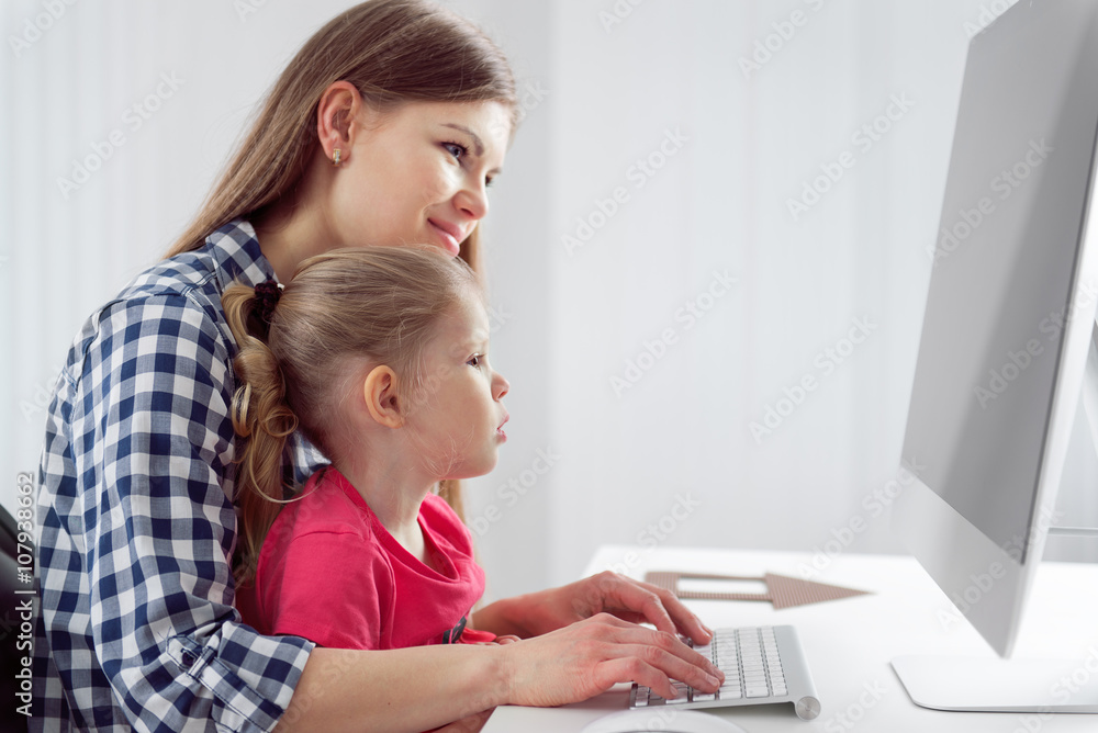 Young mom with her little girl working at computer in homeoffice. Concept of family and technology. Young mom with her little girl working at computer in homeoffice. Concept of family and technology.