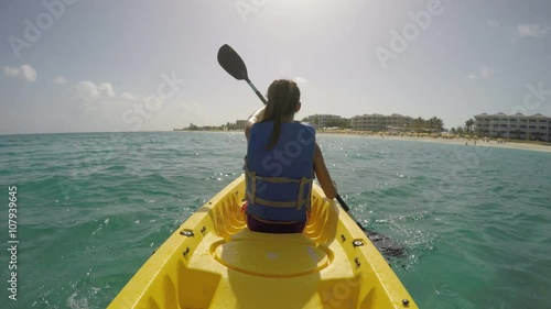 Young woman kayaking on sea against sky. Female is enjoying her summer vacations at beach. She is wearing life jacket while paddling the kayak. ACTION CAMERA.