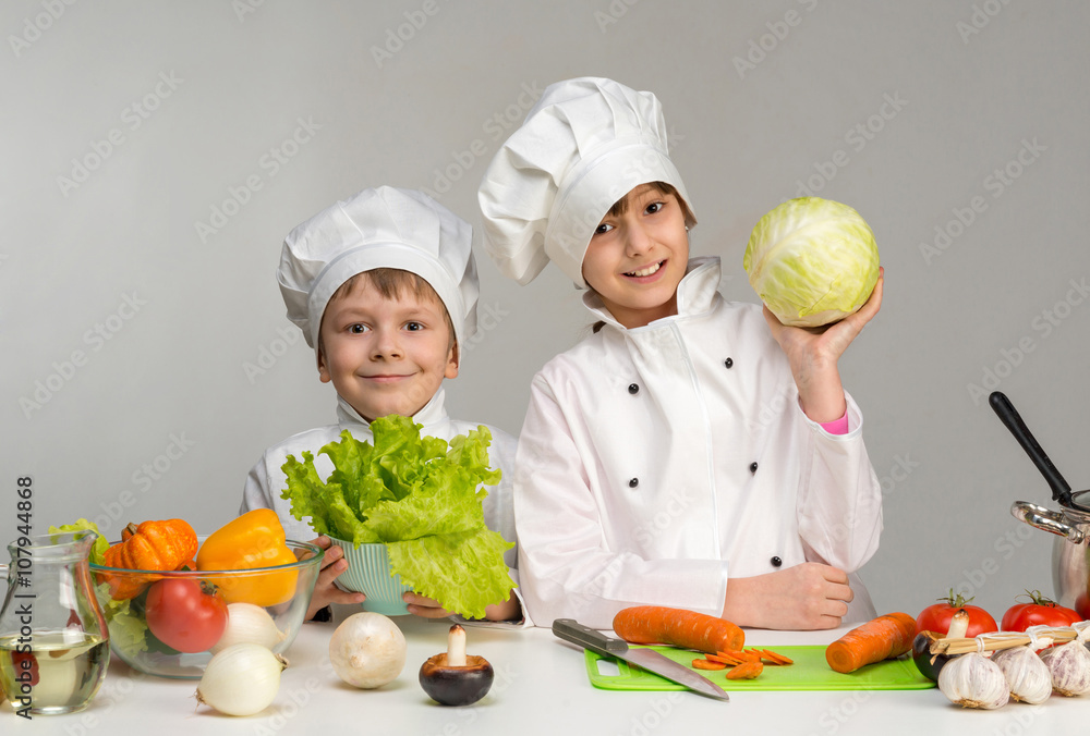 two smiling children-cooks by the table with vegetables two smiling children-cooks by the table with vegetables