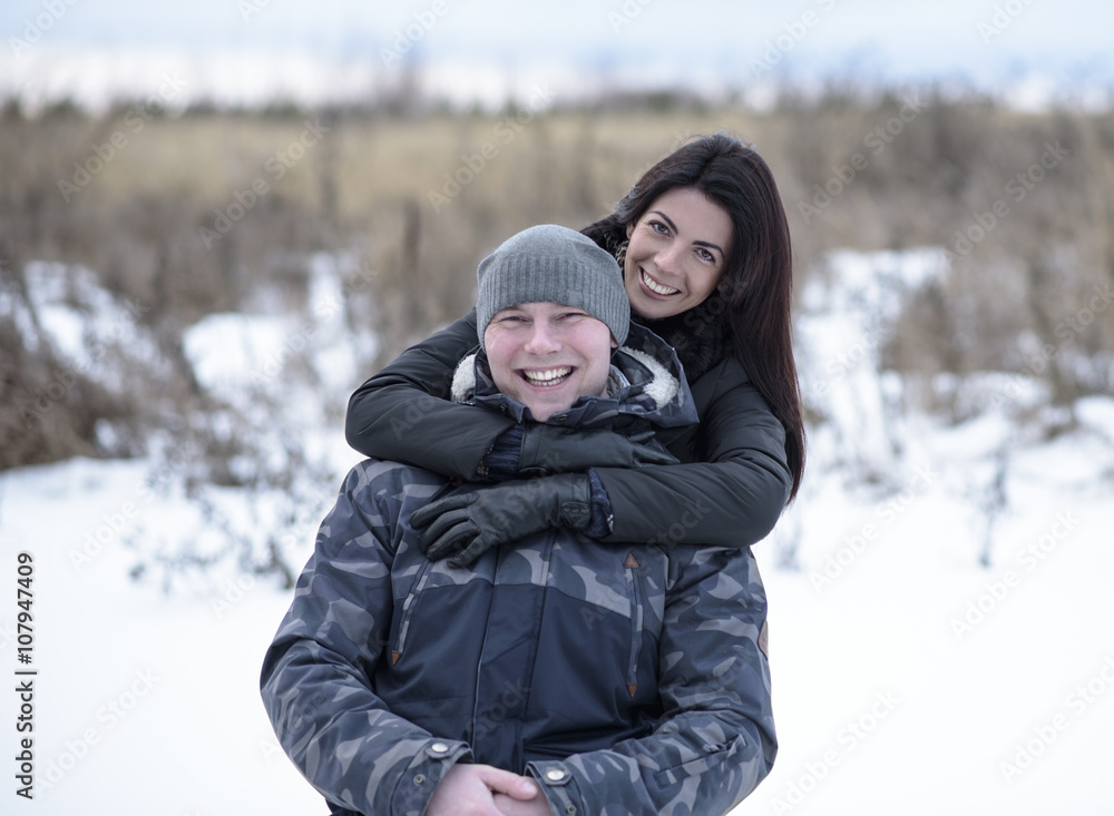 Young couple outdoors playing, cuddling in winter park. Girl hugging her boyfriend. Happy relaxing families Young couple outdoors playing, cuddling in winter park. Girl hugging her boyfriend. Happy relaxing families