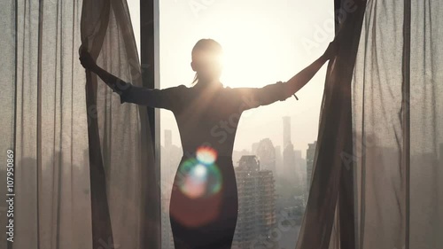 Young businesswoman unveil curtain and looking out of window
