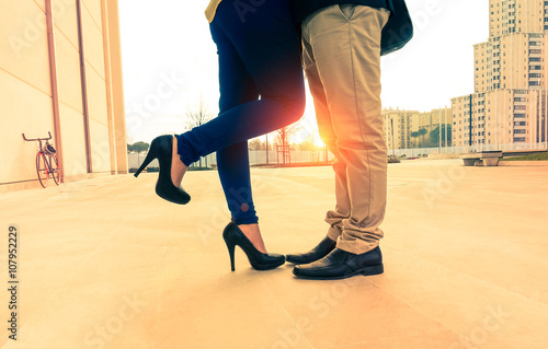 Lovers couple on date kissing and hugging on urban background at sunrise - Man and woman legs closeup outdoor - Concept of a romantic love story with vintage nostalgic filter look and warm tone
