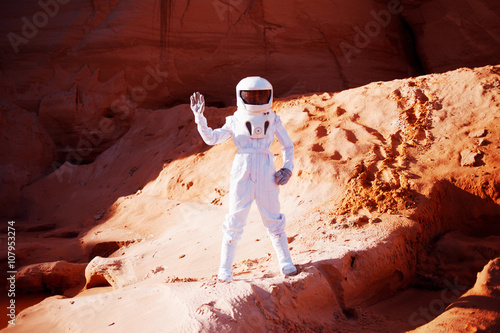 Futuristic astronaut  on  sandy planet, waving at the camera. Image with effect of toning