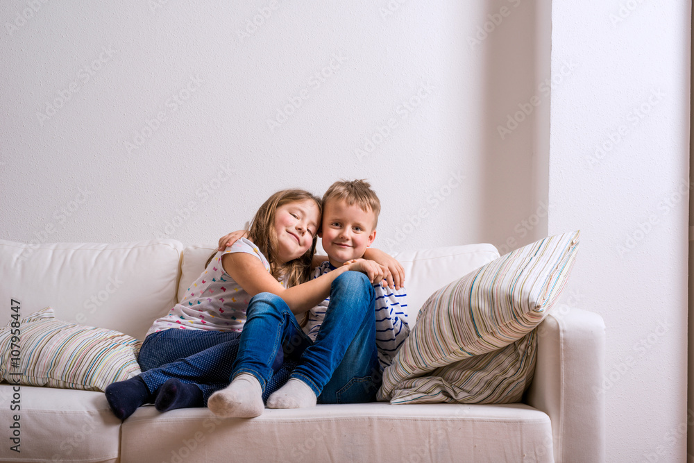 Boy and girl sitting on white couch. Copy space.