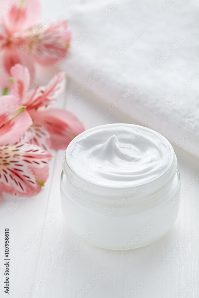 Anti wrinkle anti-aging cosmetic cream face care hygiene moisture lotion with herbal flowers therapy in glass jar with towel on white background Anti wrinkle anti-aging cosmetic cream face care hygiene moisture lotion with herbal flowers therapy in glass jar with towel on white background