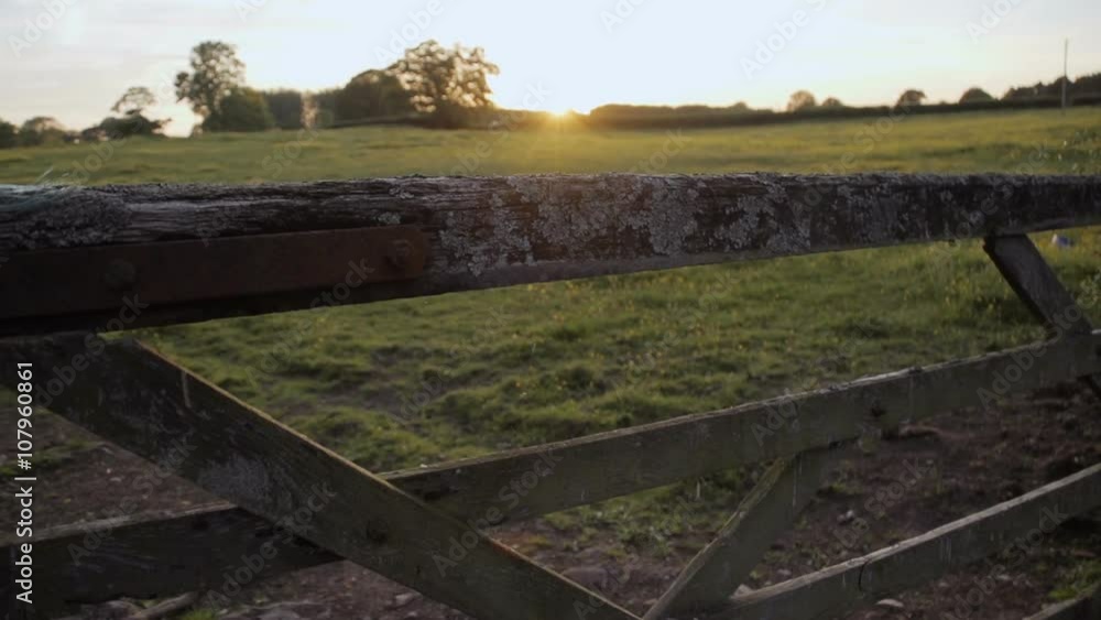 A sliding shot of the camera moving through an old wooden gate leading to a meadow at sunset. A sliding shot of the camera moving through an old wooden gate leading to a meadow at sunset.