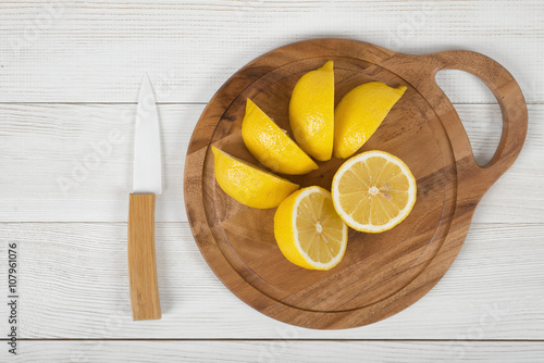 Sliced and whole lemons on cutting board with a knife next to it in top view