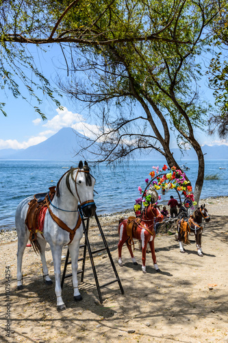 Local families relax at Lake Atitlan, Guatemala with San Pedro volcano behind. Parents pay for children to sit on life size model horses.