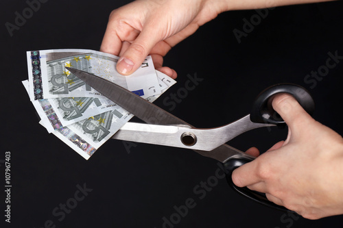 Hands with scissors cutting Euro banknotes, on black background © Africa Studio