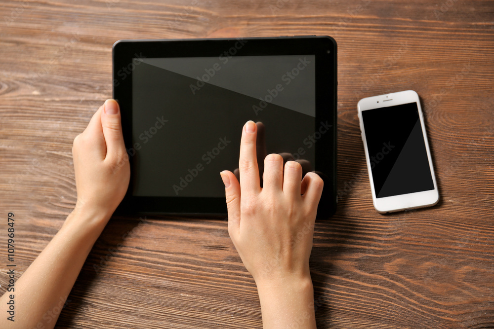 Mobile phone and female hands using tablet, on the wooden background Mobile phone and female hands using tablet, on the wooden background