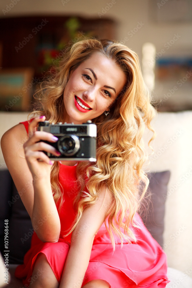 Smiling woman in dress with retro camera, on couch at home Smiling woman in dress with retro camera, on couch at home