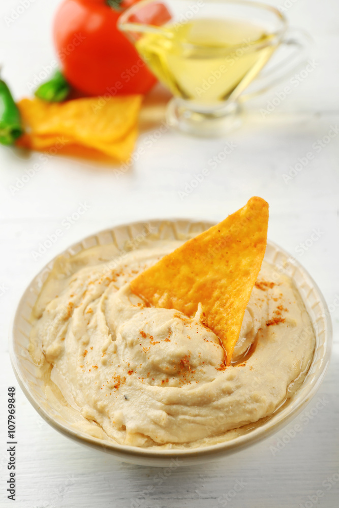 Ceramic bowl of tasty hummus with chips and oil on table