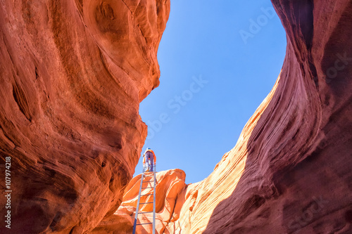 Hiker climbs a tall ladder to exit a red sandstone slot canyon in Arizona