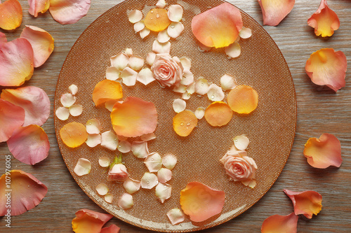 Pink and yellow rose petals in golden bowl with water on wooden background