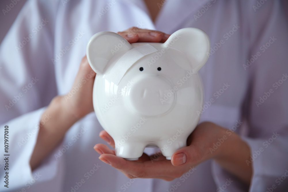 Woman holding in hands white piggy bank with patch Woman holding in hands white piggy bank with patch