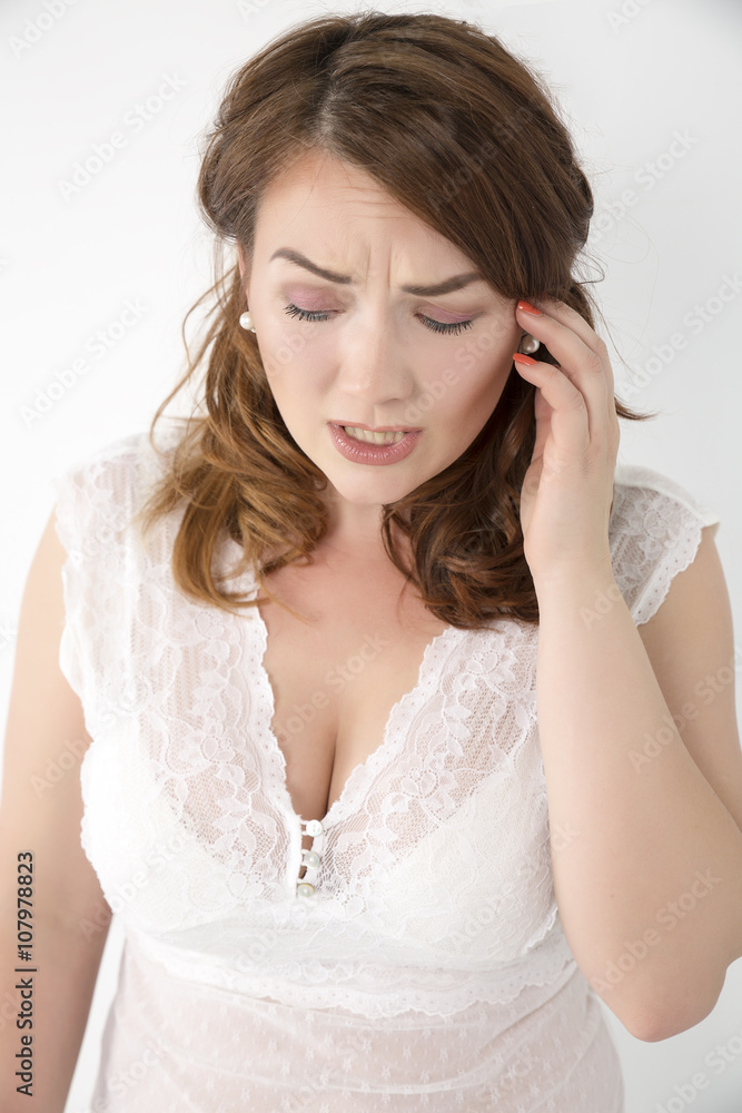 Close-up portrait of the emotional beautiful girl touching hand to head and looks down . On a white background . Close-up portrait of the emotional beautiful girl touching hand to head and looks down . On a white background .