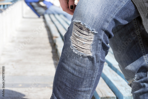 Ripped jeans on knee of the girl teenager sitting outdoor early spring.