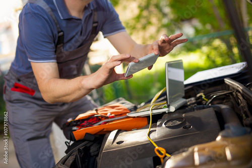 Professional car mechanic working in auto repair service, photographing damage on the car