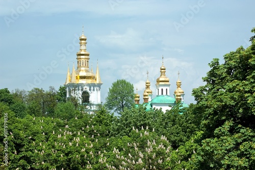 Gilded domes of Christian Orthdox churches of Kyiv Pechersk Lavra peek out from behind the blooming chestnut trees in Kyiv, Ukraine photo