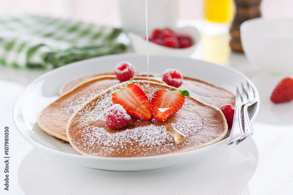 Homemade buttermilk american pancakes with fresh strawberry, raspberry and honey on a white plate on a white table for breakfast, closeup, selective focus.. Homemade buttermilk american pancakes with fresh strawberry, raspberry and honey on a white plate on a white table for breakfast, closeup, selective focus..