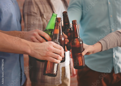 Male group clinking glass bottles of beer, close up