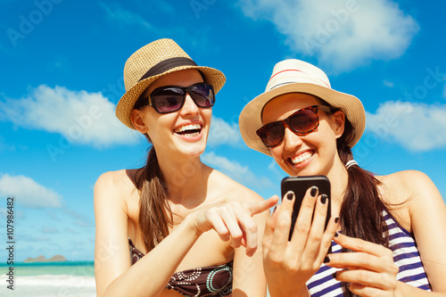 Pretty girls using smart phone on the beach. Summer holiday, technology and beach concept.   © kieferpix