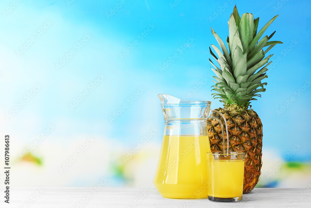 Fresh pineapple juice in glass and pitcher on blue background Fresh pineapple juice in glass and pitcher on blue background