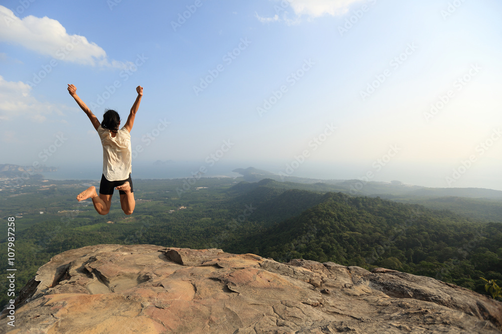  cheering young asian woman jumping on mountain peak rock