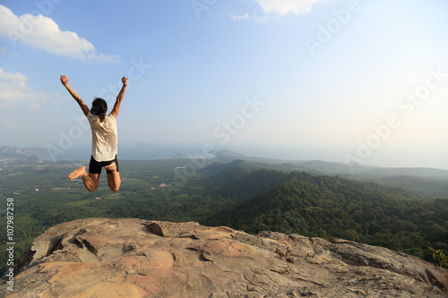  cheering young asian woman jumping on mountain peak rock