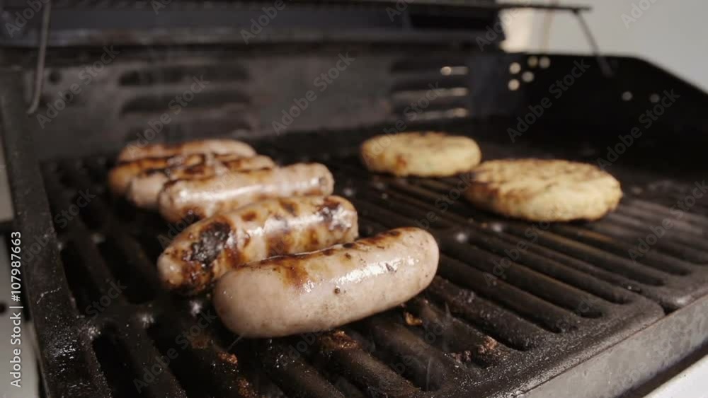 Slow motion shot of sausages sizzling away on the BBQ with Burgers and Veggie Burgers cooking away. Fantastic detail of fat bubbling and smoke wafting off the char-grilled meet. Slow motion shot of sausages sizzling away on the BBQ with Burgers and Veggie Burgers cooking away. Fantastic detail of fat bubbling and smoke wafting off the char-grilled meet.