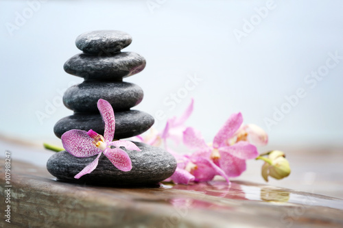Stack of spa stones with pink orchids on wooden wet bridge